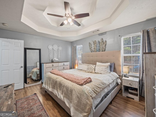 bedroom with multiple windows, a raised ceiling, visible vents, and wood finished floors