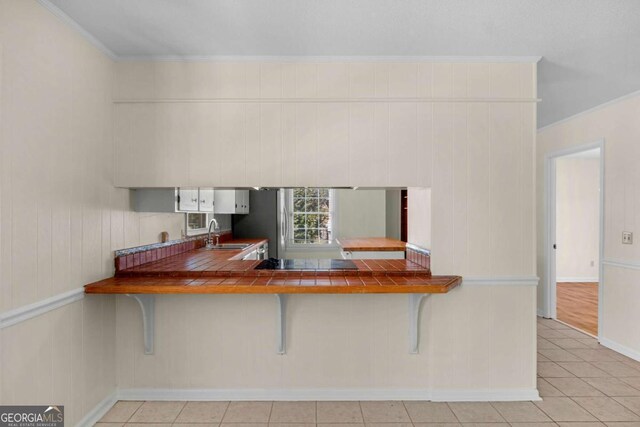 kitchen with crown molding, black electric stovetop, tile counters, a kitchen bar, and a sink