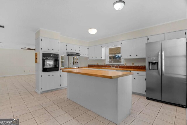 kitchen with light tile patterned floors, a sink, white cabinets, black oven, and stainless steel fridge