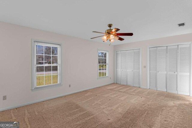 unfurnished bedroom with visible vents, carpet flooring, multiple closets, and ceiling fan