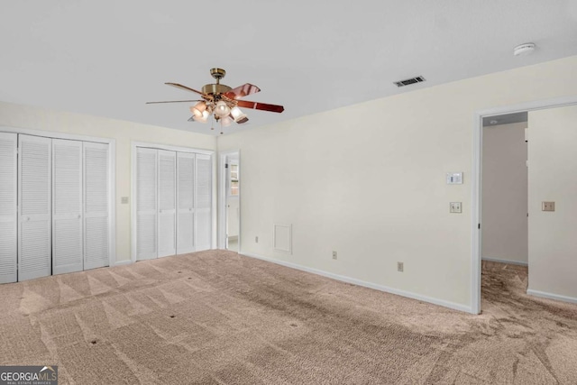 unfurnished bedroom featuring a ceiling fan, visible vents, baseboards, carpet floors, and multiple closets