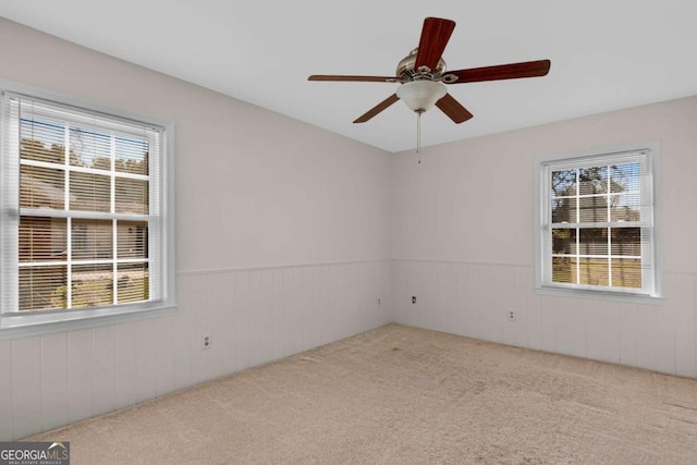 carpeted empty room with a ceiling fan and wainscoting