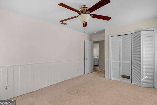 unfurnished bedroom featuring visible vents, carpet, wainscoting, a closet, and a ceiling fan