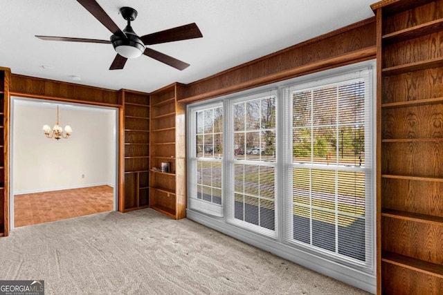 empty room featuring ceiling fan with notable chandelier, plenty of natural light, carpet, and wood walls