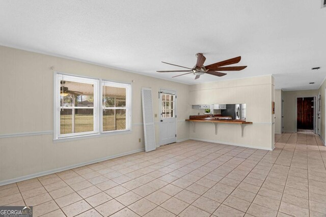 unfurnished living room featuring light tile patterned flooring, a textured ceiling, baseboards, and a ceiling fan