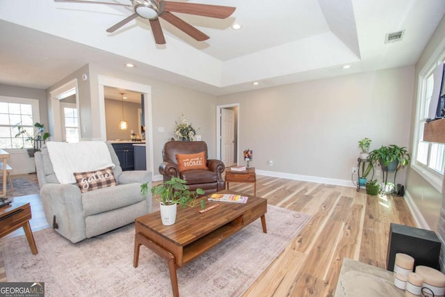 living room with light wood-type flooring, visible vents, baseboards, and a tray ceiling