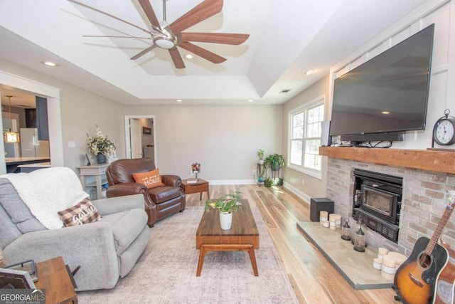 living room featuring light wood-type flooring, a tray ceiling, recessed lighting, baseboards, and ceiling fan