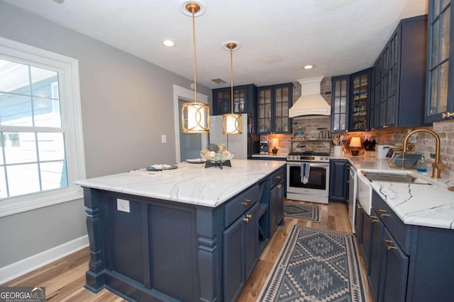 kitchen with a kitchen island, blue cabinetry, custom range hood, appliances with stainless steel finishes, and tasteful backsplash