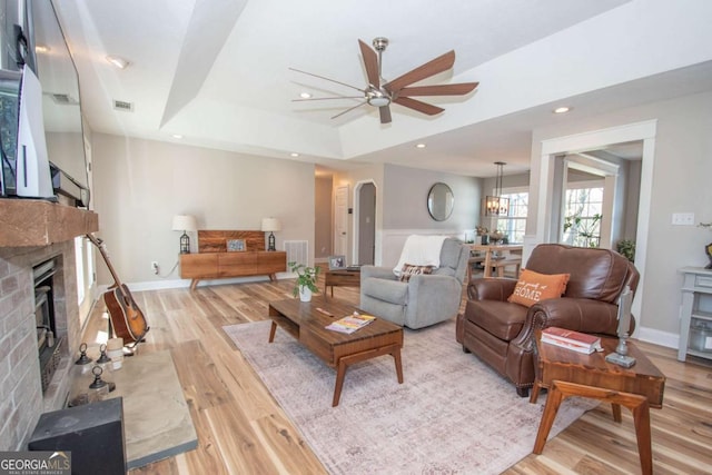 living area with a tray ceiling, a brick fireplace, visible vents, and light wood-type flooring