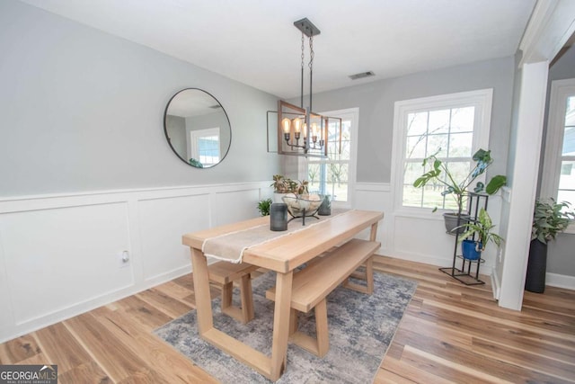 dining space featuring light wood-type flooring, visible vents, a notable chandelier, and wainscoting