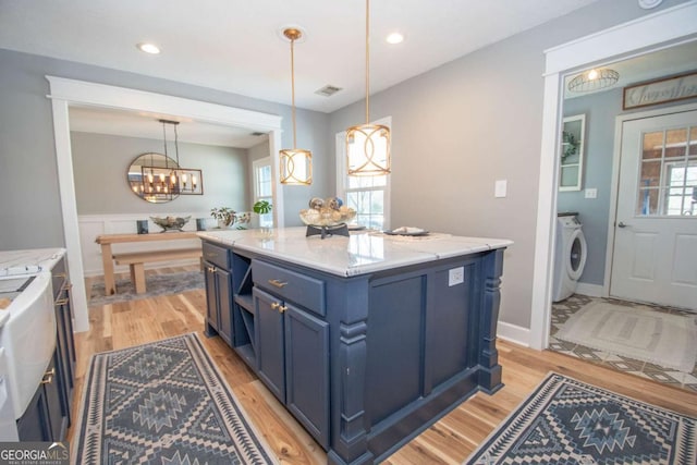 kitchen with washer / clothes dryer, blue cabinets, light wood-style floors, and light stone countertops