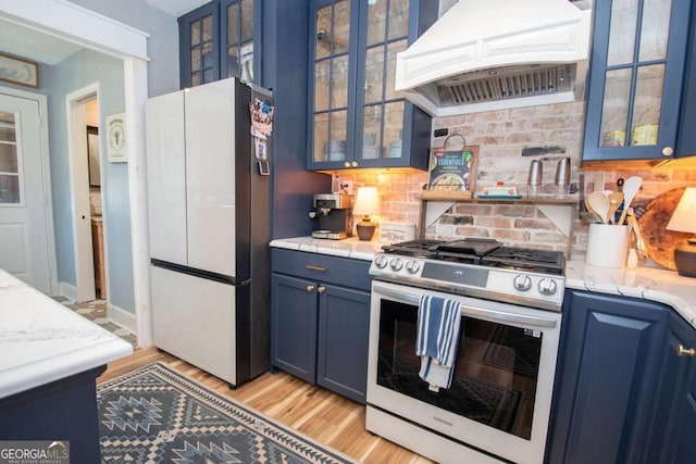 kitchen featuring blue cabinets, custom exhaust hood, stainless steel gas range, and freestanding refrigerator