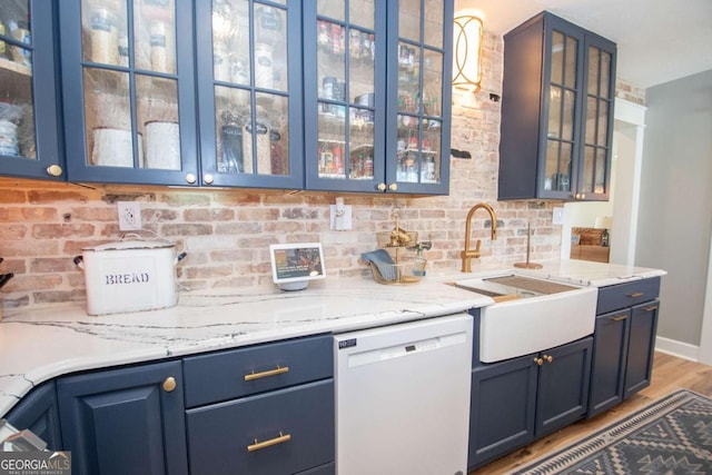 kitchen featuring blue cabinets, a sink, white dishwasher, glass insert cabinets, and light stone countertops