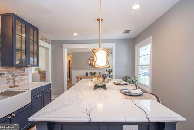 kitchen with blue cabinets, visible vents, decorative backsplash, a center island, and glass insert cabinets