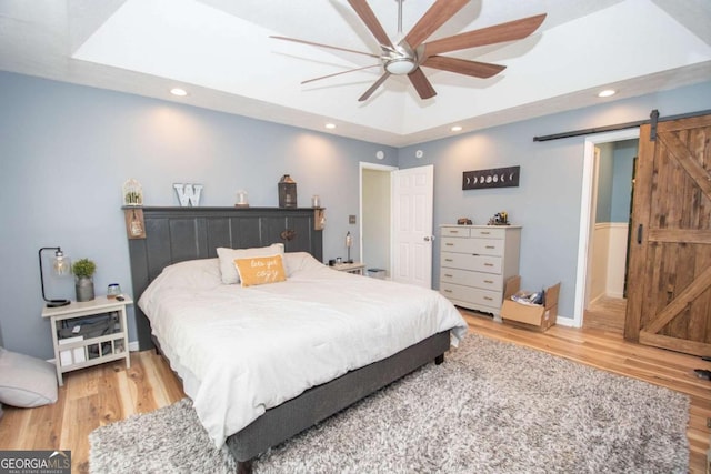 bedroom with recessed lighting, light wood-style flooring, a tray ceiling, and a barn door