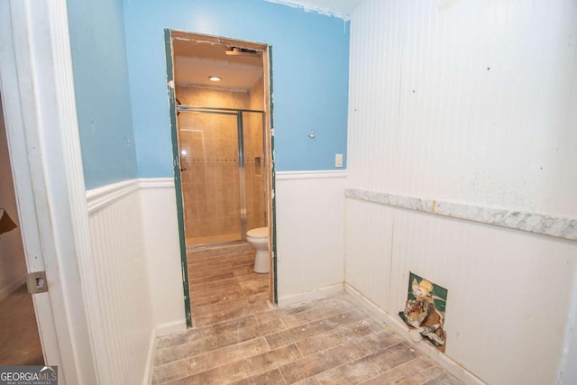 full bathroom featuring a shower stall, toilet, wood finished floors, and a wainscoted wall