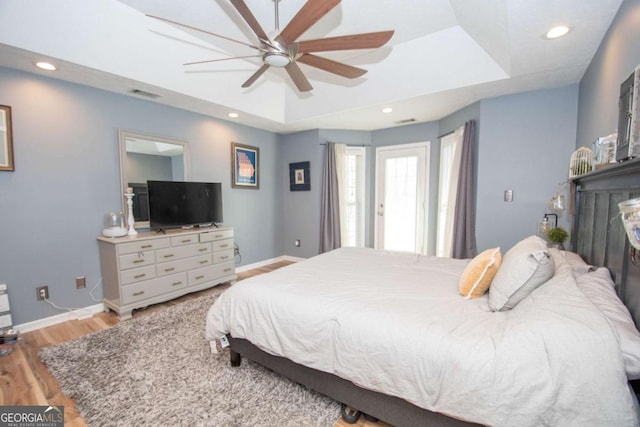 bedroom featuring visible vents, a raised ceiling, baseboards, and wood finished floors