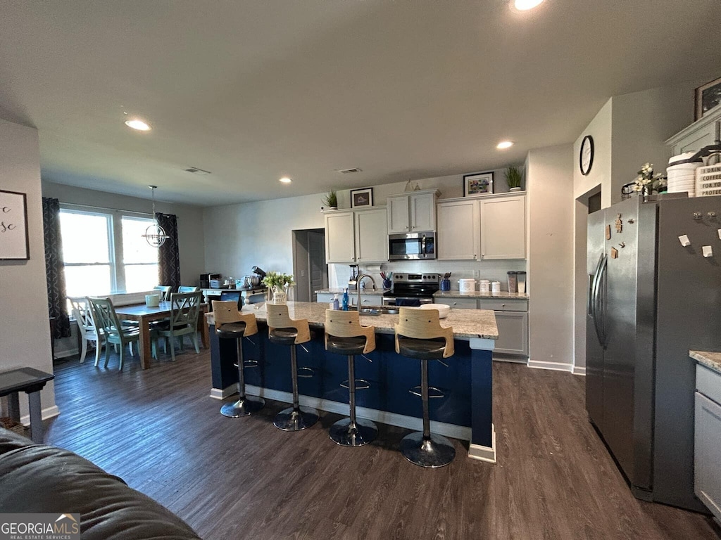 kitchen with a kitchen bar, dark wood-type flooring, a sink, recessed lighting, and stainless steel appliances