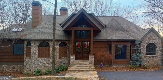 view of front of house featuring stone siding, french doors, a chimney, and roof with shingles