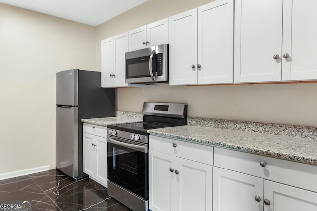 kitchen featuring baseboards, light stone countertops, white cabinets, marble finish floor, and stainless steel appliances