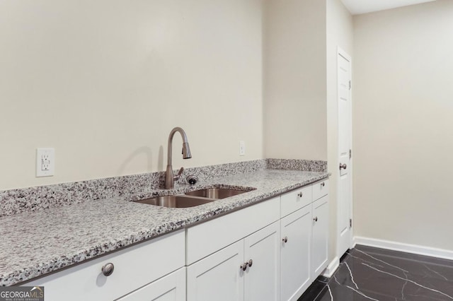 kitchen with baseboards, light stone countertops, marble finish floor, white cabinetry, and a sink