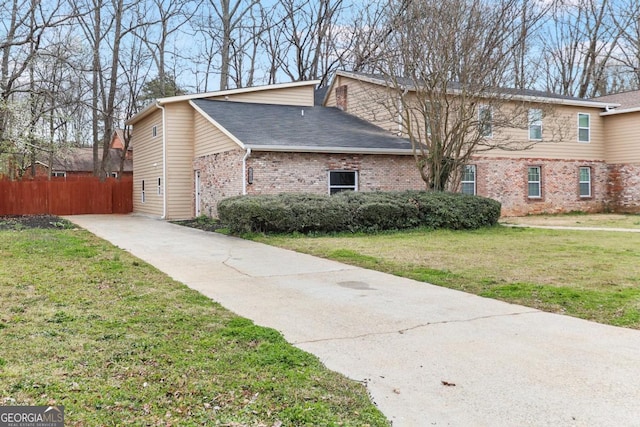 view of side of property featuring brick siding, a lawn, a shingled roof, and fence