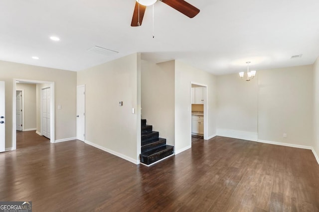 unfurnished living room with ceiling fan with notable chandelier, stairway, dark wood-style floors, and baseboards