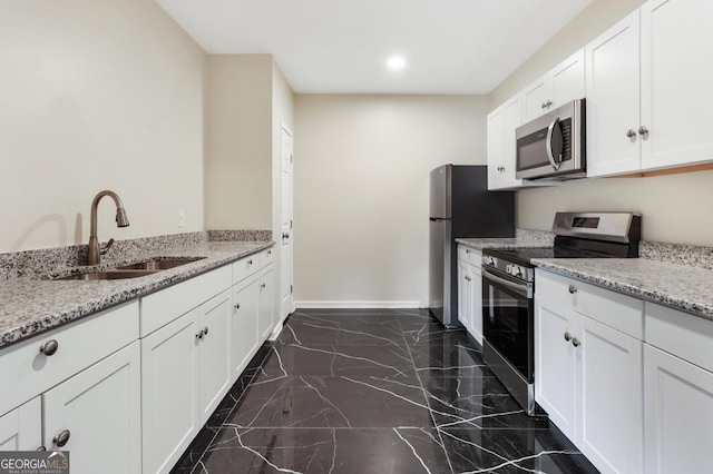 kitchen with light stone counters, a sink, appliances with stainless steel finishes, white cabinetry, and marble finish floor