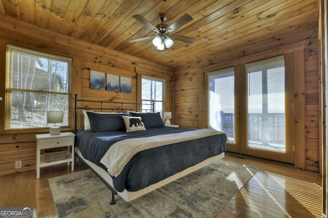 bedroom with a ceiling fan, hardwood / wood-style floors, wooden walls, wooden ceiling, and access to exterior