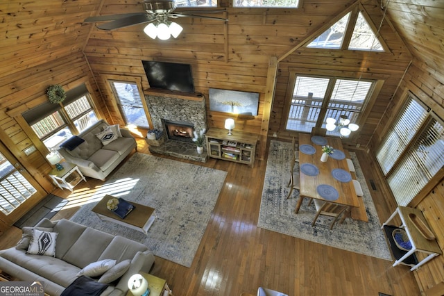 unfurnished living room featuring a stone fireplace, wood walls, high vaulted ceiling, and wood-type flooring