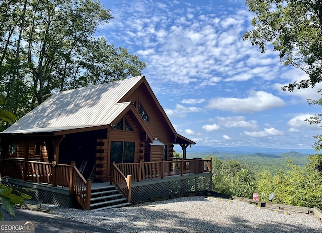 log-style house with metal roof, a view of trees, log exterior, and a mountain view