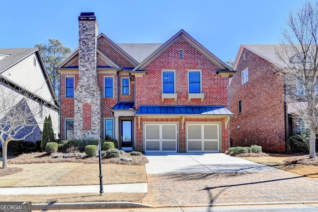 view of front facade with brick siding, driveway, a chimney, and a standing seam roof