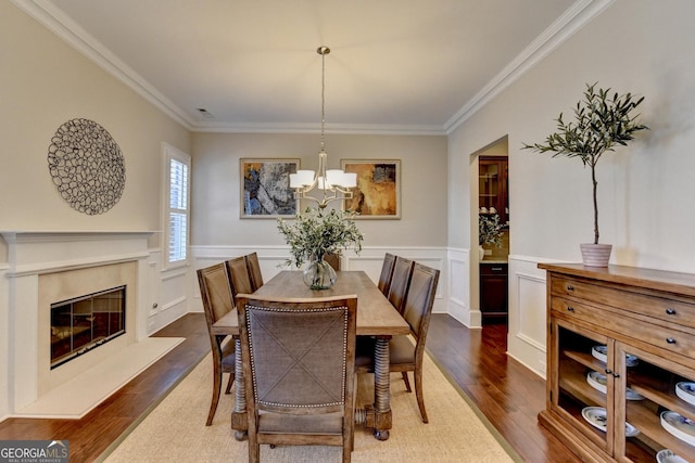 dining space with dark wood-type flooring, a fireplace, a wainscoted wall, and ornamental molding