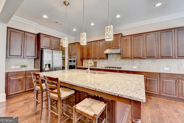 kitchen with light wood finished floors, a sink, stainless steel appliances, under cabinet range hood, and crown molding