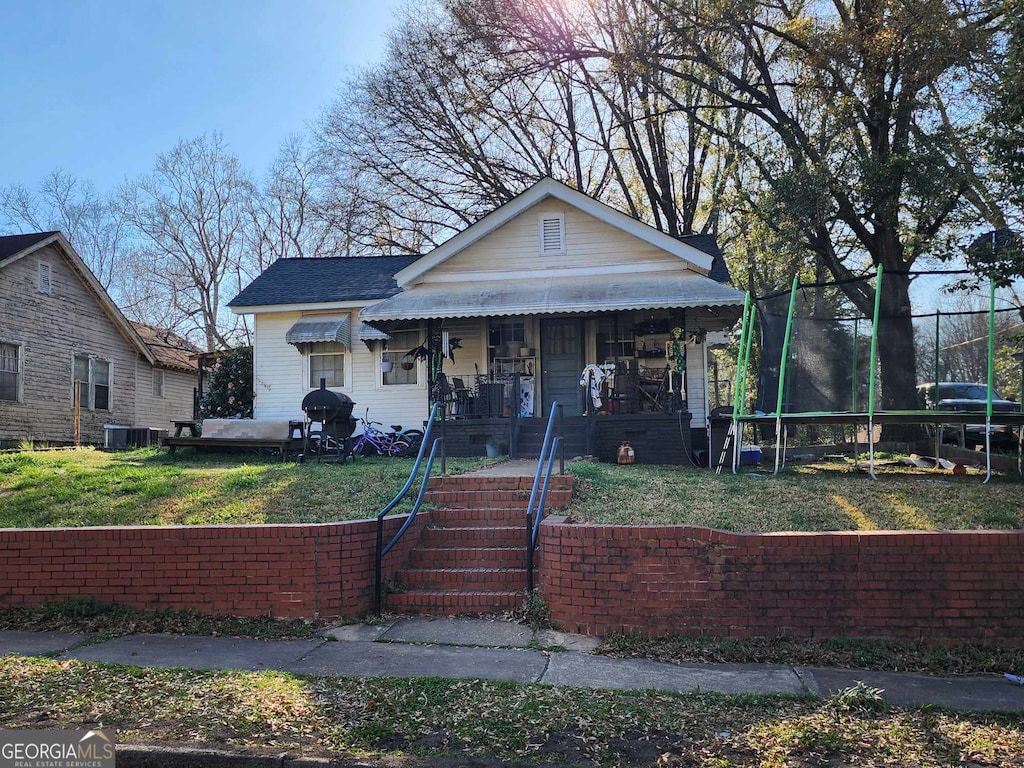 bungalow-style home with a trampoline, covered porch, and central AC