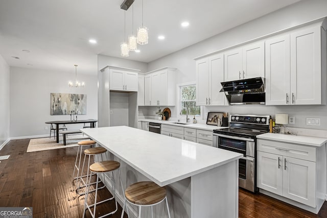 kitchen with dark wood-type flooring, a sink, a kitchen island, appliances with stainless steel finishes, and wall chimney exhaust hood