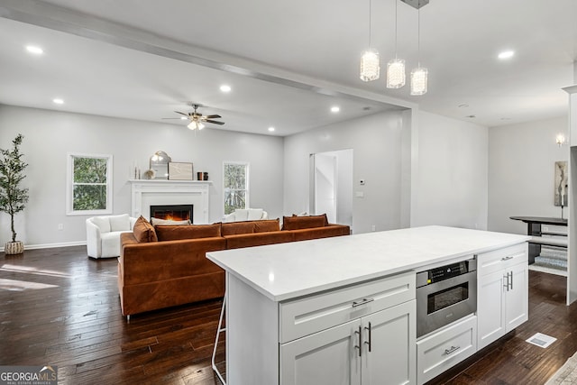 kitchen featuring recessed lighting, dark wood-style flooring, a lit fireplace, white cabinets, and a center island