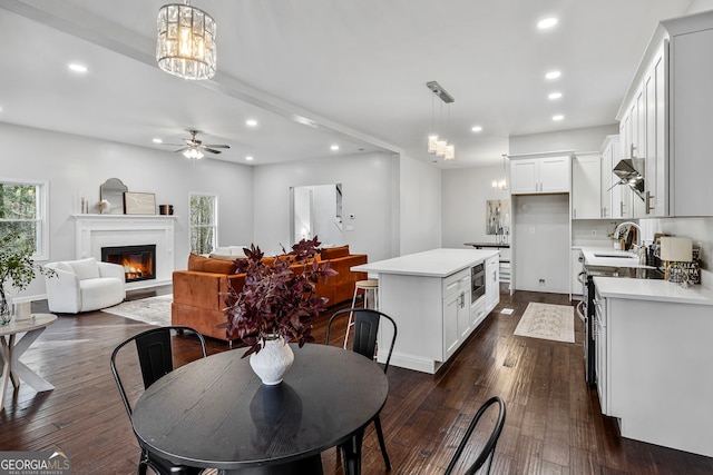 dining area featuring dark wood finished floors, a glass covered fireplace, ceiling fan with notable chandelier, and recessed lighting