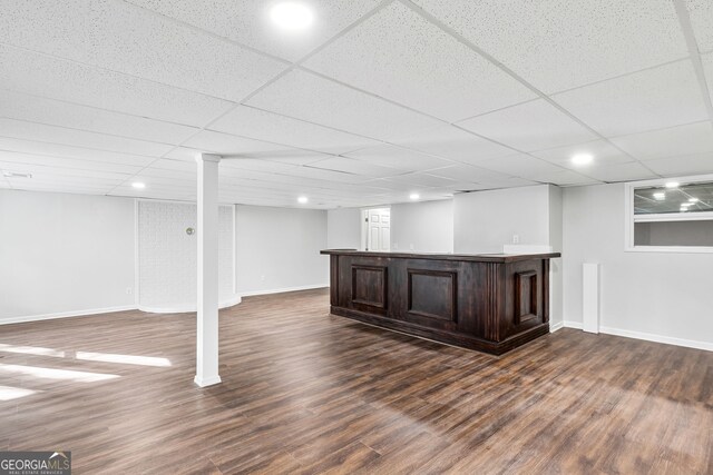 finished below grade area featuring a paneled ceiling, bar area, baseboards, and dark wood-style flooring