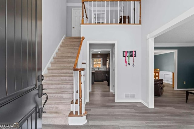 entryway with stairs, visible vents, wood finished floors, and crown molding