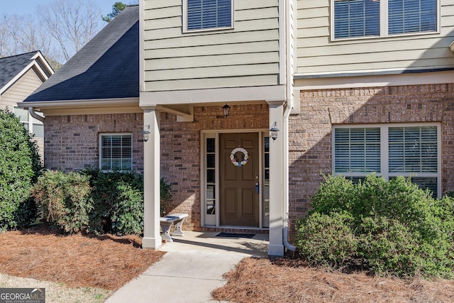 doorway to property with brick siding and a shingled roof