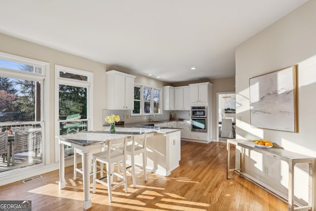 kitchen featuring light wood finished floors, stainless steel double oven, a peninsula, decorative backsplash, and white cabinets