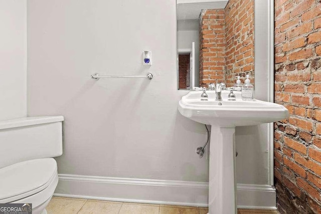 bathroom with toilet, a sink, brick wall, tile patterned flooring, and baseboards