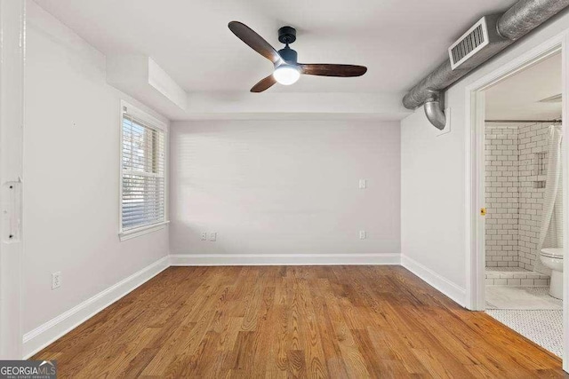 unfurnished bedroom featuring visible vents, ensuite bath, wood finished floors, baseboards, and ceiling fan