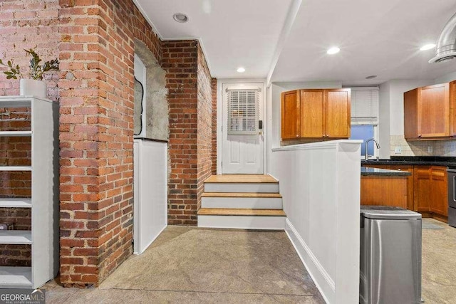 kitchen with dark countertops, brown cabinets, brick wall, and a sink