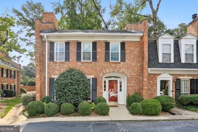 view of front of house with brick siding, a chimney, and a shingled roof