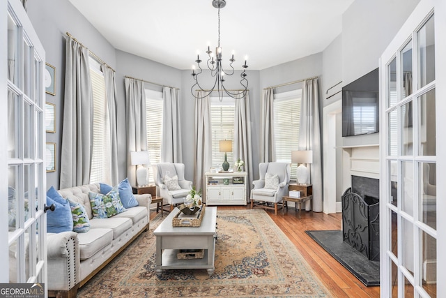 living area featuring a notable chandelier, plenty of natural light, a fireplace, and wood finished floors