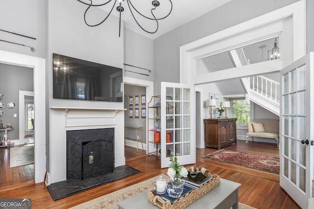 living area with a fireplace with raised hearth, french doors, high vaulted ceiling, and hardwood / wood-style flooring