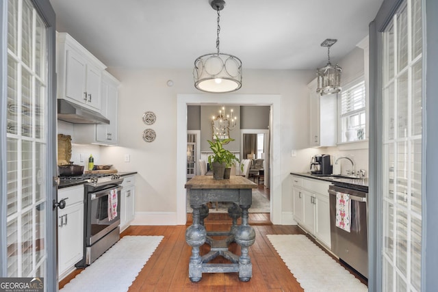 kitchen with an inviting chandelier, a sink, stainless steel appliances, under cabinet range hood, and dark countertops