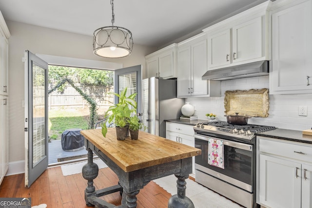 kitchen with dark countertops, backsplash, under cabinet range hood, and stainless steel appliances